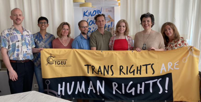 TLN meeting participants hold a banner that says, 'Trans rights are human rights'