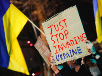 A protester holds a cardboard banner that says 'Just stop invading Ukraine'