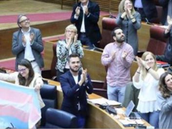 People applauding in Valencia Parliament. Among them, the former vice-president of the Generalitat and spokesperson for Compromís coalition, Mónica Oltra, raises the trans flag.