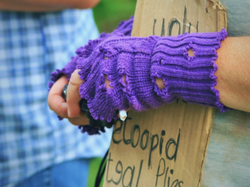 Hands of a young person wearing purple fingerless gloves and holding a cardboard banner