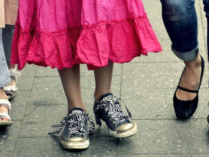 Feet of a person walking: they are wearing black sneakers with zebra shoelaces and a long pink skirt