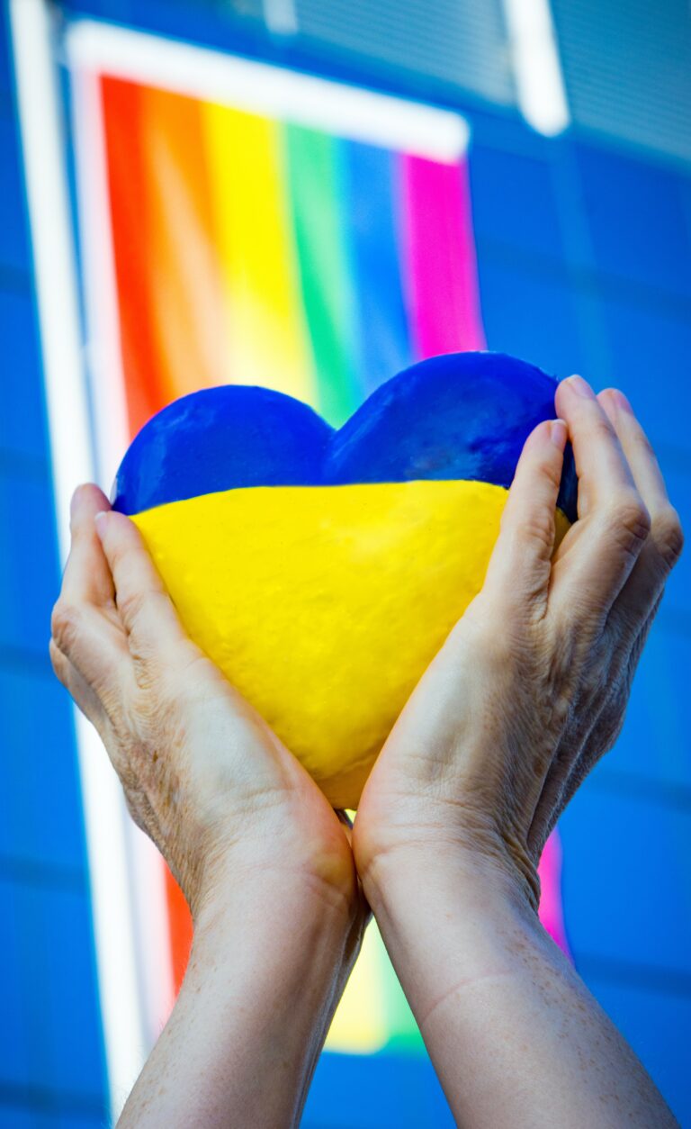 Hands hold a heart in Ukrainian colors, with a rainbow flag backdrop. Photo by Marek Studzinski.