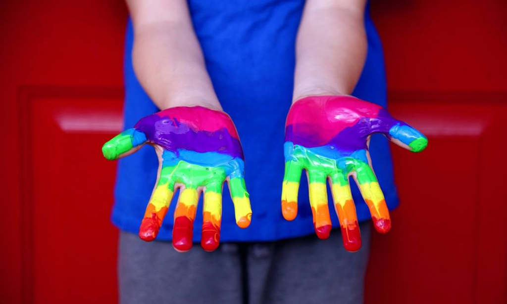 Two hands with rainbow colors painted on their palms.