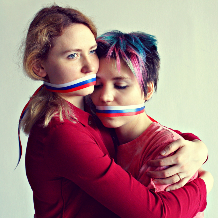 Two white people in red hug with ribbons of white, blue, and red covering their mouths.