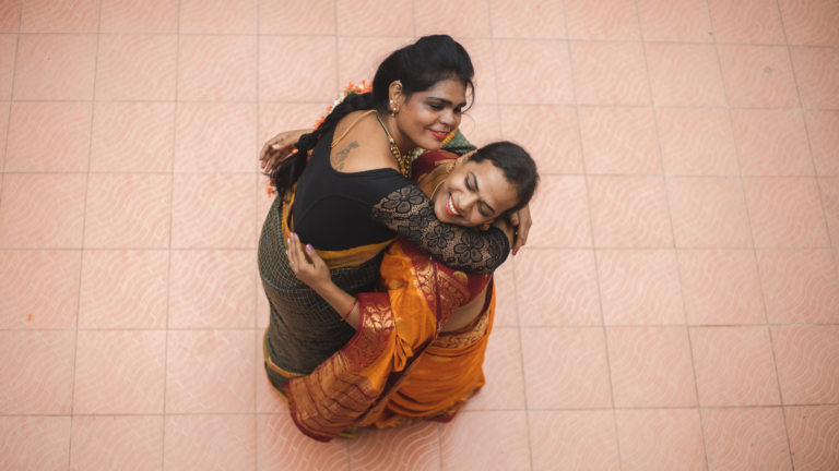 Two trans women in saris embrace.