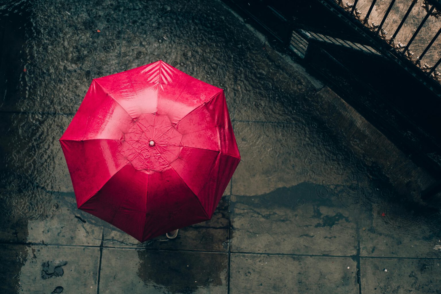 Ariel view of a person holding a red umbrella in the rain. the person is not visible