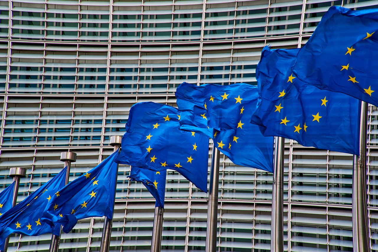 Several EU flags waving in the wind in front of an office building