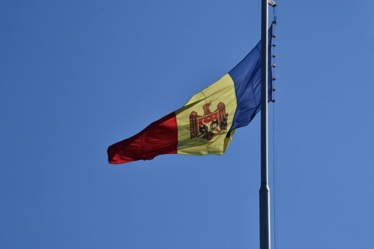 Romanian flag, including coat of arms, flying high against a blue sky