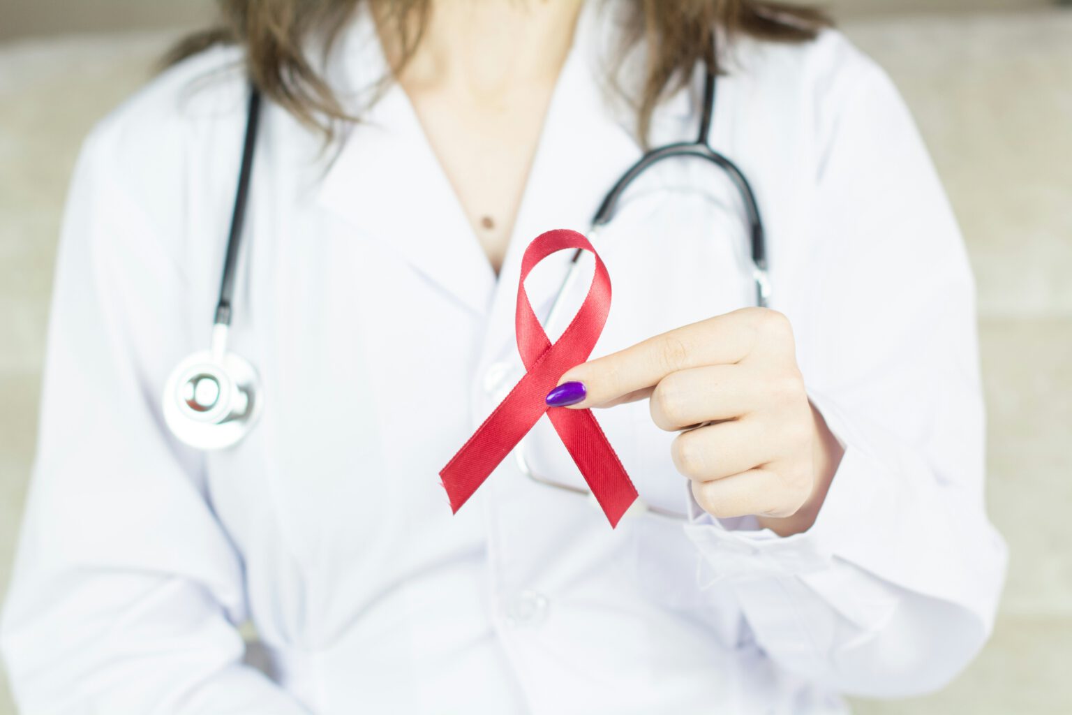 Medical professional in a white coat, holding a red ribbon for AIDS